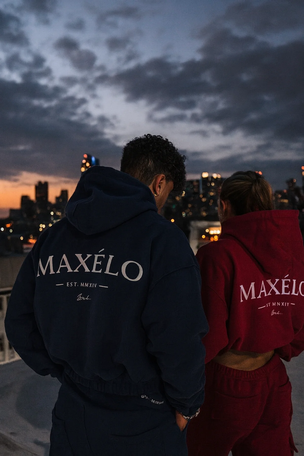 Two models wearing navy and red MAXÉLO hoodies in a city setting